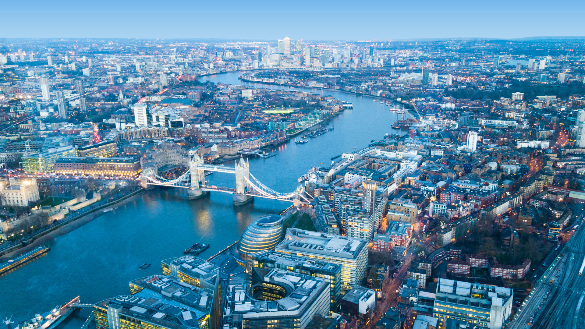Aerial view of London at dusk featuring Tower Bridge and the River Thames surrounded by the city skyline.